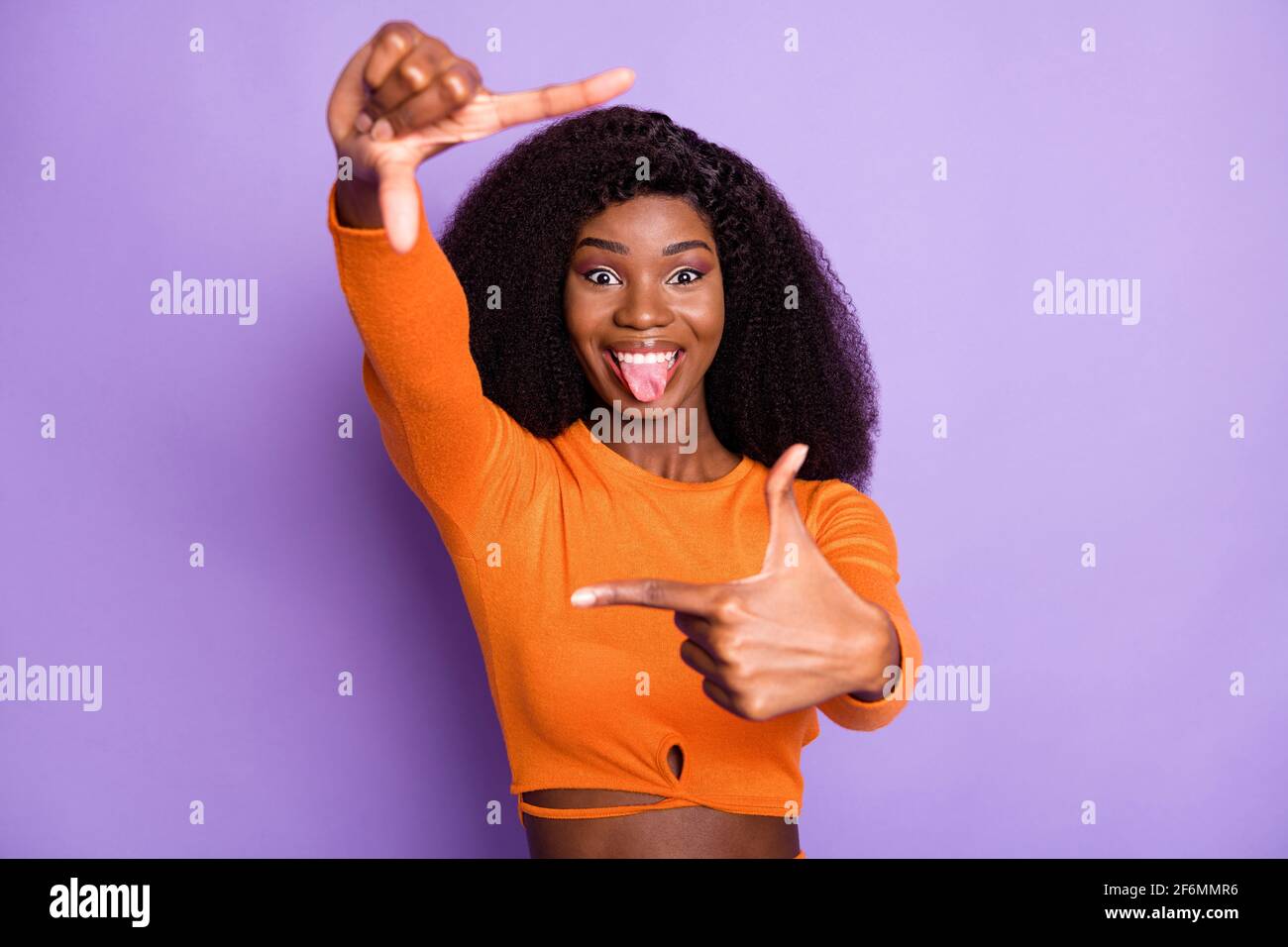 Ritratto di bella ragazza allegra e allegra con capelli ondulati che mostra grimacing cornice isolato su sfondo color viola pastello Foto Stock