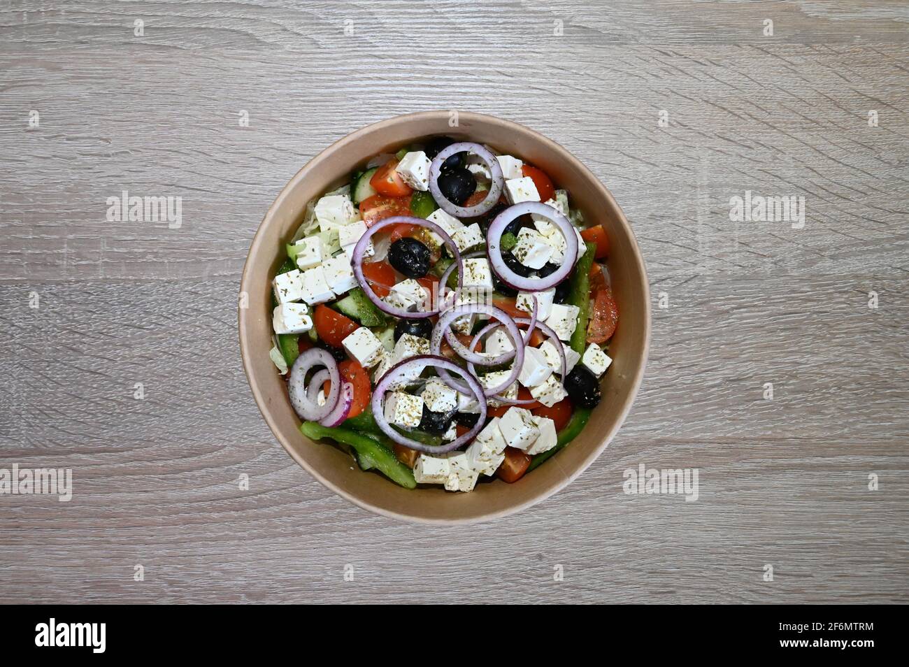 Insalata greca tradizionale in una ciotola posta su un tavolo di legno con condimento greco fatto in casa come parte della dieta mediterranea. Foto Stock