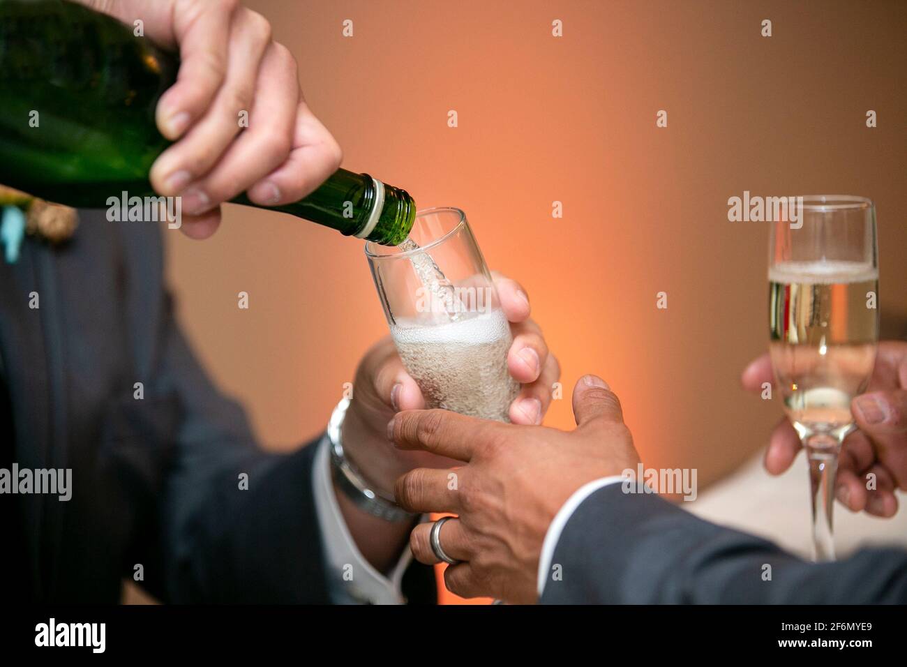 Due uomini versando Champaigne in bicchieri a stelo e condividendo con festeggia un matrimonio Foto Stock