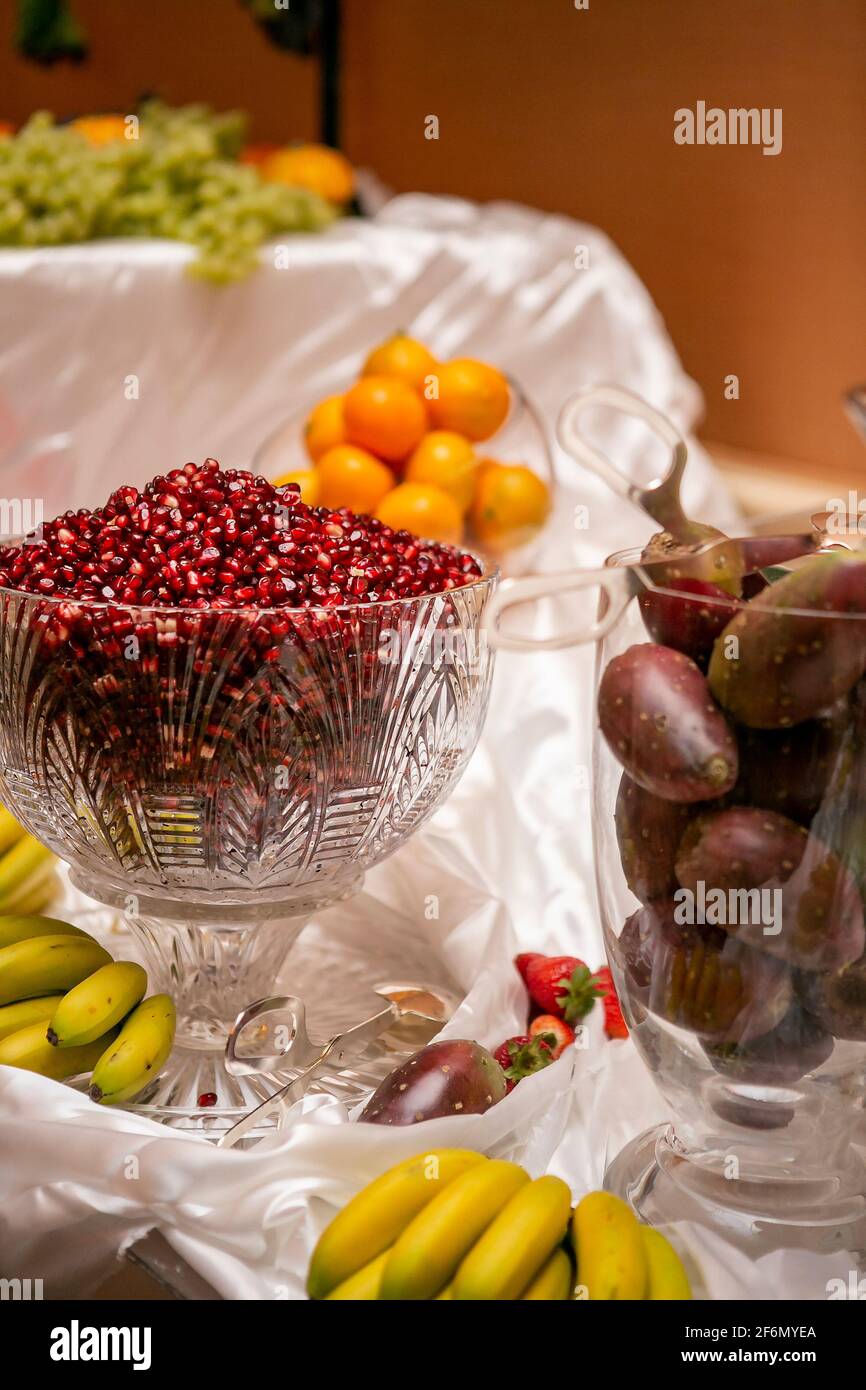 Tavola piena di frutti in recipienti contenenti semi di melograno, arance, pere di ceci, banane, fragole e uve; catering per una cerimonia nuziale Foto Stock