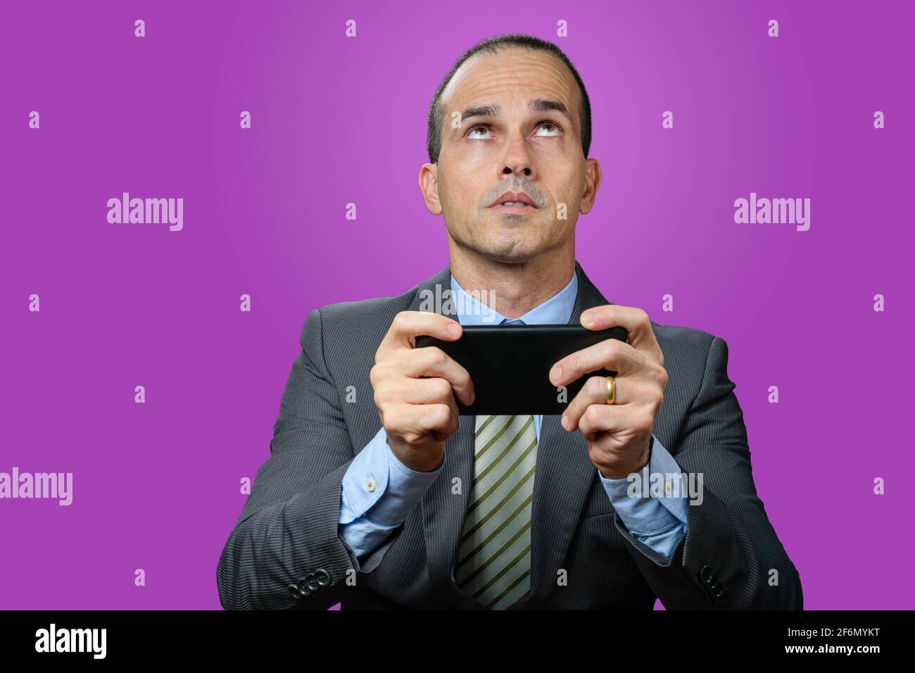 Uomo maturo con abito e cravatta, tenendo il suo smartphone in orizzontale, preoccupato e guardando in alto. Foto Stock