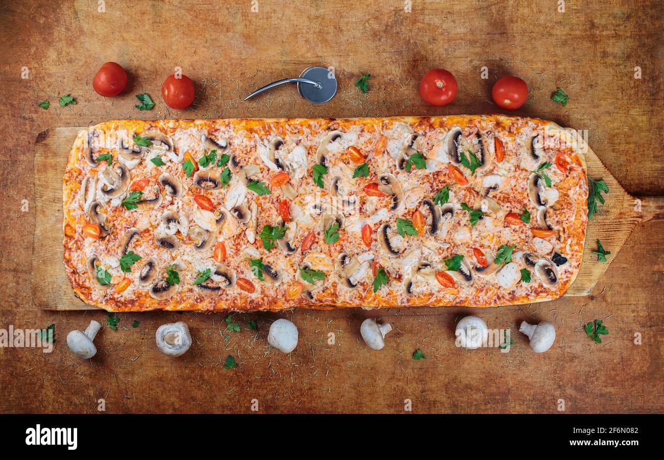 La pizza lunga con scalino e funghi si trova su un tavolo di legno. Pizza romana su una spatola di legno. Pizza. Lunga un metro sulla spatola di legno per pizza. Foto Stock