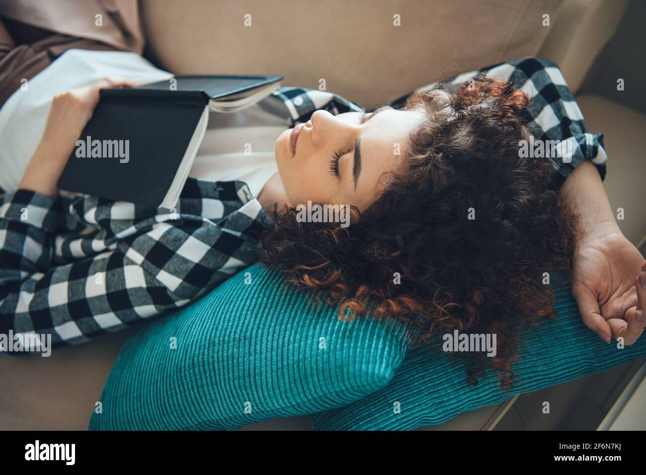 La donna con capelli ricci stanchi è sdraiata su un divano e. napping dopo la lettura di un libro Foto Stock