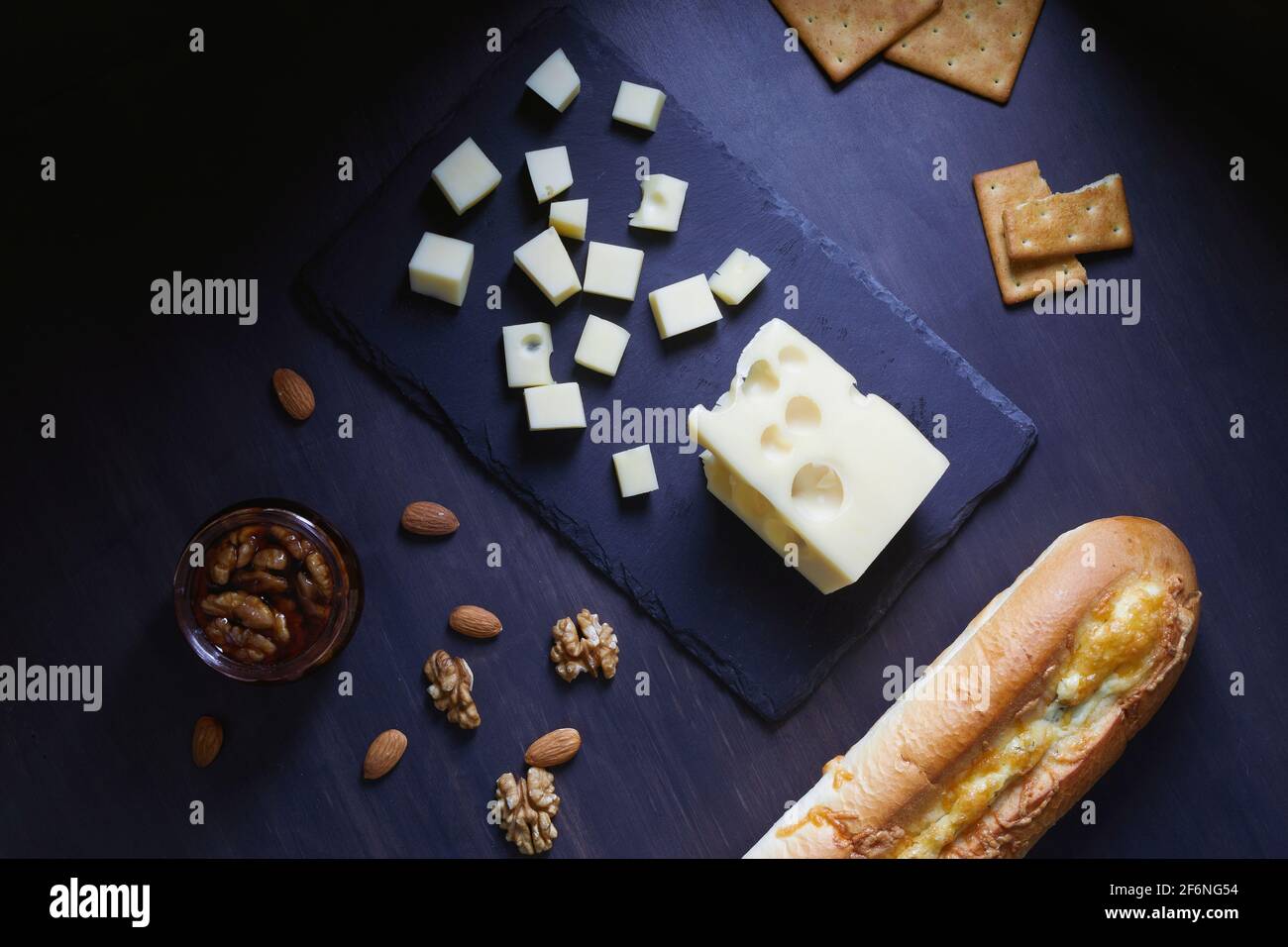 Formaggio Maasdam con noci, miele, baguette e cracker su fondo piatto di pietra nera. Foto Stock