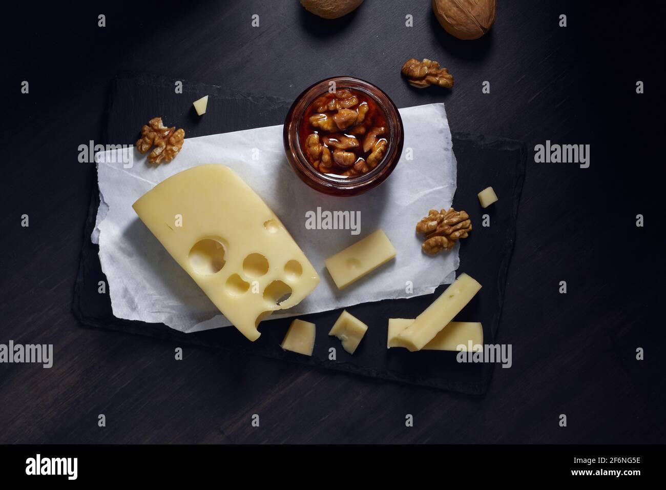 il formaggio tagliato a fette giace su un piatto di pietra con miele e noce su sfondo scuro. Vista dall'alto Foto Stock
