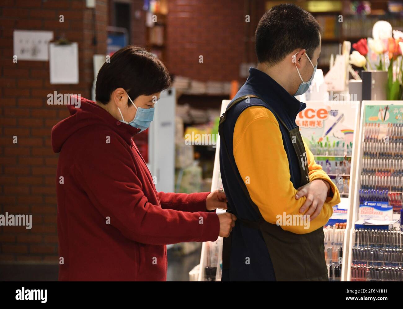 (210402) -- PECHINO, 2 aprile 2021 (Xinhua) -- la madre di Kang Rui (L) aiuta Kang a mettere la sua uniforme alla Foreign Language Teaching and Research Press (FLTRP) Bookstore a Pechino, capitale della Cina, 2 aprile 2021. Kang Rui, 22 anni, è un poster designer di Foreign Language Teaching and Research Press (FLTRP) Bookstore a Pechino. Diagnosticato con autismo a cinque anni e mezzo, Kang Rui è stato inviato a studiare in un centro di istruzione speciale per i bambini autistici, dove ha fatto grandi progressi nelle abilità di apprendimento e di vita. Con la compagnia della sua famiglia, Kang ha finito la scuola superiore professionale Foto Stock