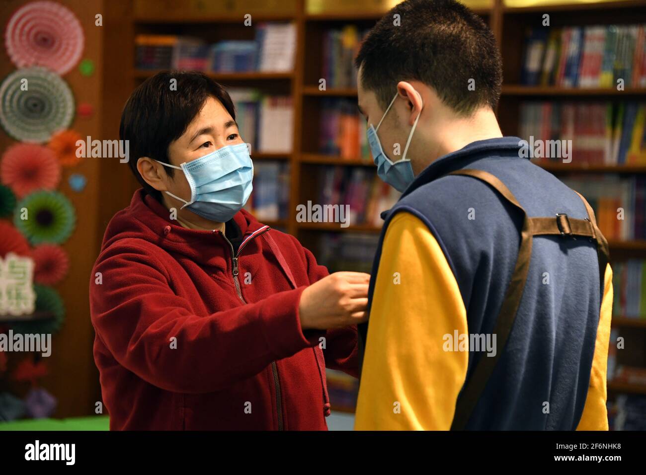 (210402) -- PECHINO, 2 aprile 2021 (Xinhua) -- la madre di Kang Rui (L) aiuta Kang a mettere la sua uniforme alla Foreign Language Teaching and Research Press (FLTRP) Bookstore a Pechino, capitale della Cina, 2 aprile 2021. Kang Rui, 22 anni, è un poster designer di Foreign Language Teaching and Research Press (FLTRP) Bookstore a Pechino. Diagnosticato con autismo a cinque anni e mezzo, Kang Rui è stato inviato a studiare in un centro di istruzione speciale per i bambini autistici, dove ha fatto grandi progressi nelle abilità di apprendimento e di vita. Con la compagnia della sua famiglia, Kang ha finito la scuola superiore professionale Foto Stock