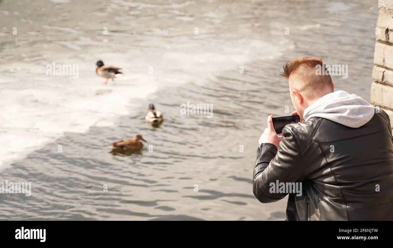 Un giovane scatta foto di anatre sull'acqua. Vista dal retro. Foto Stock
