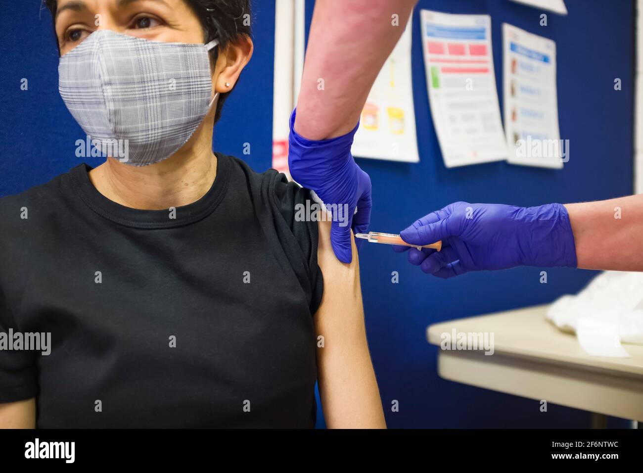 Donna asiatica britannica che indossa una maschera facciale, ottenendo un vaccino Covid 19 in un centro di vaccinazione in Inghilterra, Regno Unito Foto Stock