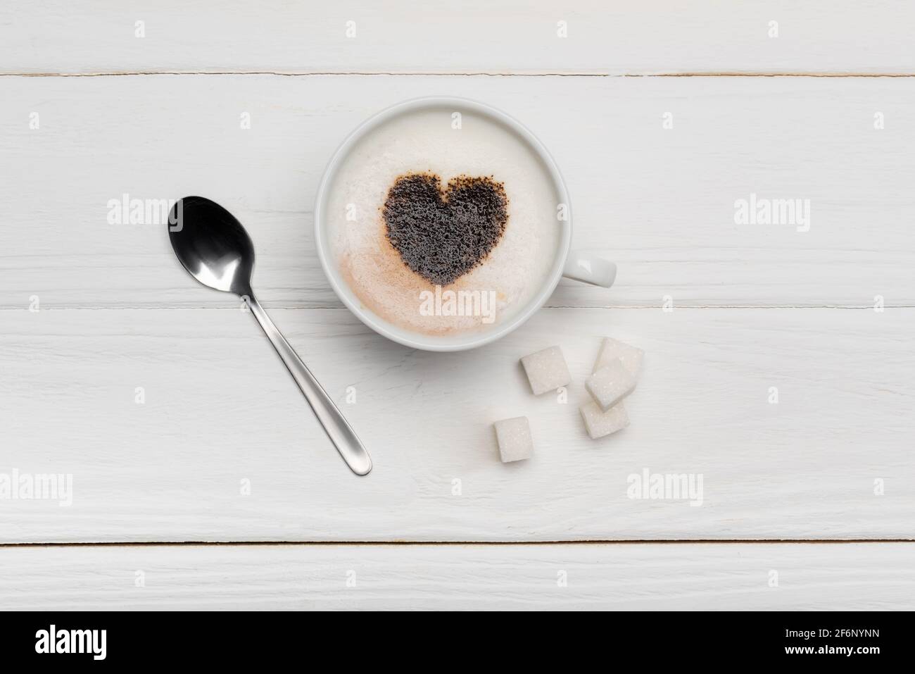 vista dall'alto della tazza con cappuccino vicino al cucchiaio e zucchero cubetti su sfondo bianco di legno Foto Stock
