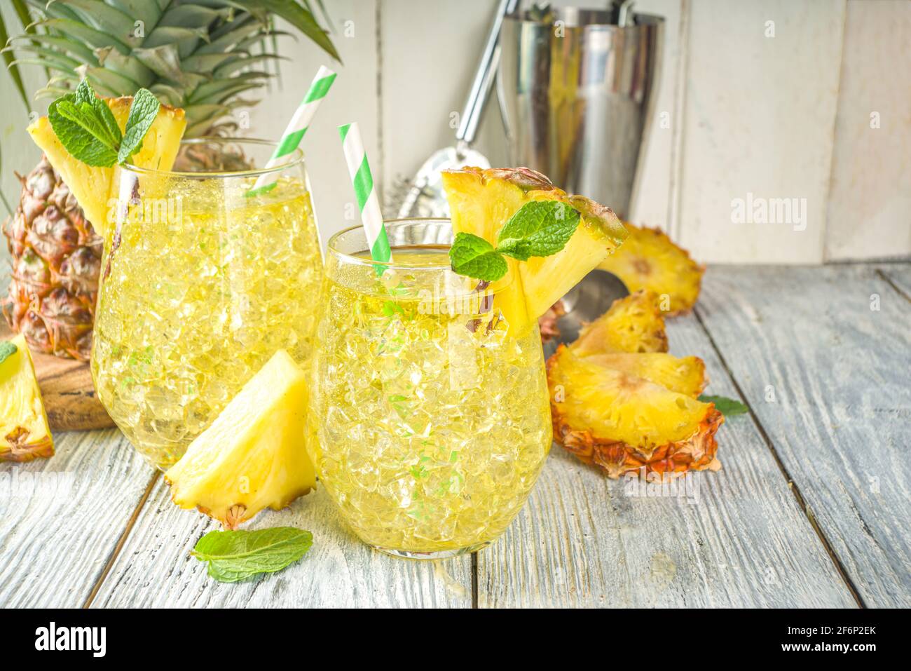 Bevanda all'ananas e al lime, cocktail alla limonata con ananas tagliato e fette, su sfondo bianco di legno con foglie tropicali e tondini copia sp Foto Stock