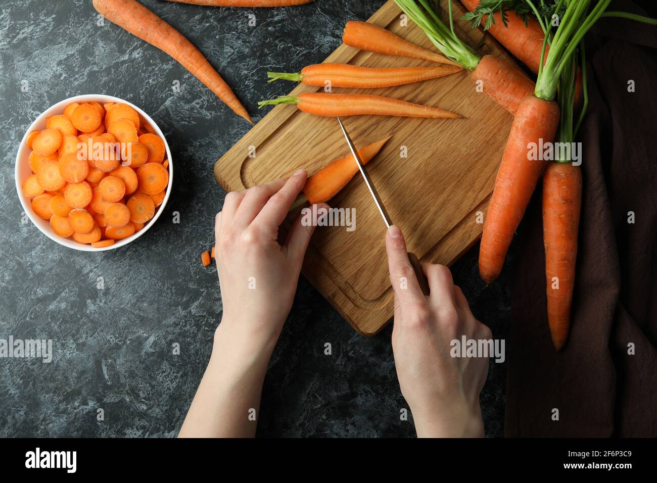 Donna taglia carote su tavola di legno su sfondo nero di fumé Foto