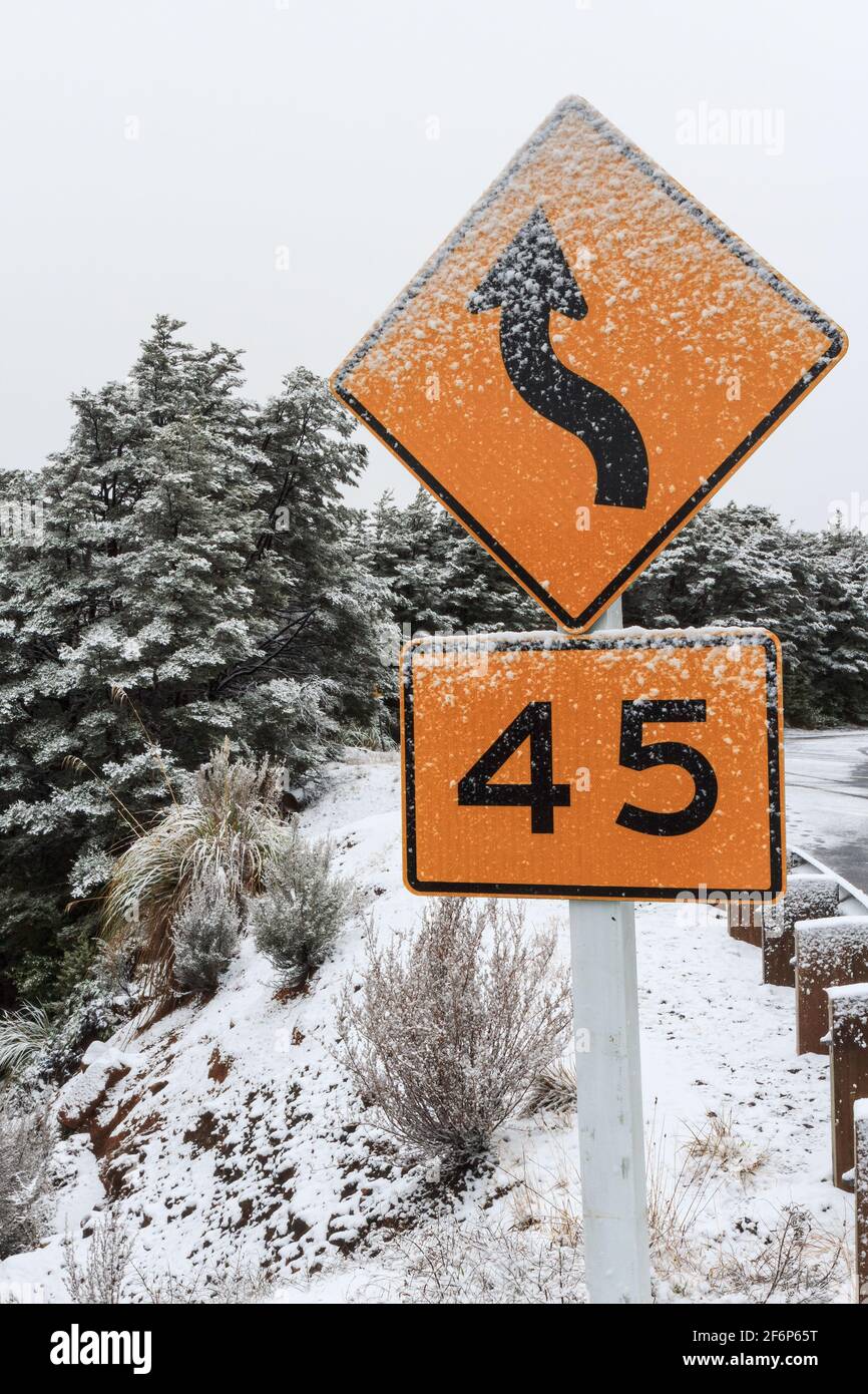 Una strada tortuosa e un segnale limite di velocità di 45 kp/h su una montagna innevata. Monte Ruapehu, Nuova Zelanda Foto Stock