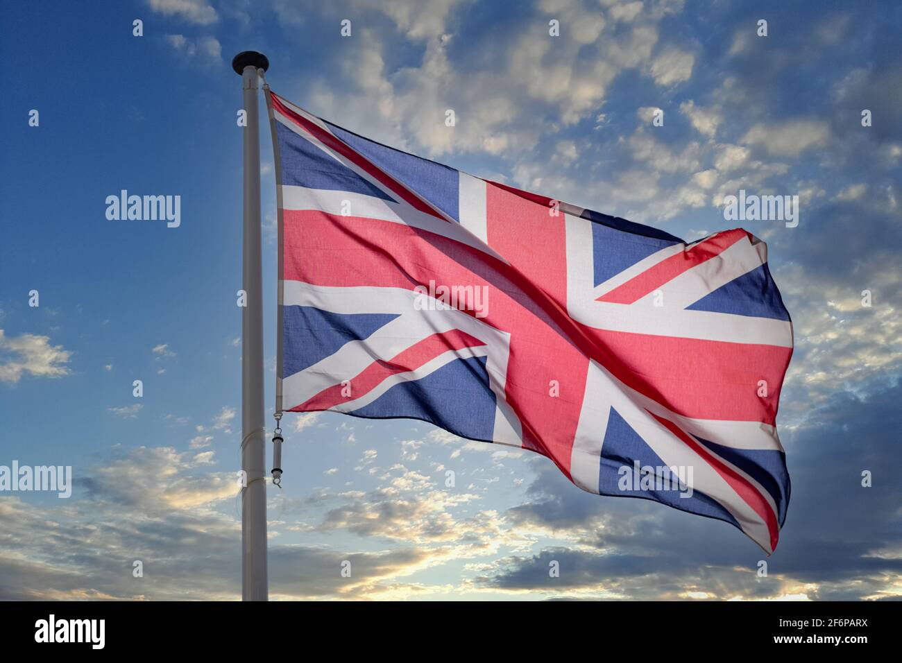 Bandiera britannica, Regno Unito simbolo nazionale della Gran Bretagna e dell'Irlanda del Nord su un palo che oscilla contro il cielo blu nuvoloso Foto Stock