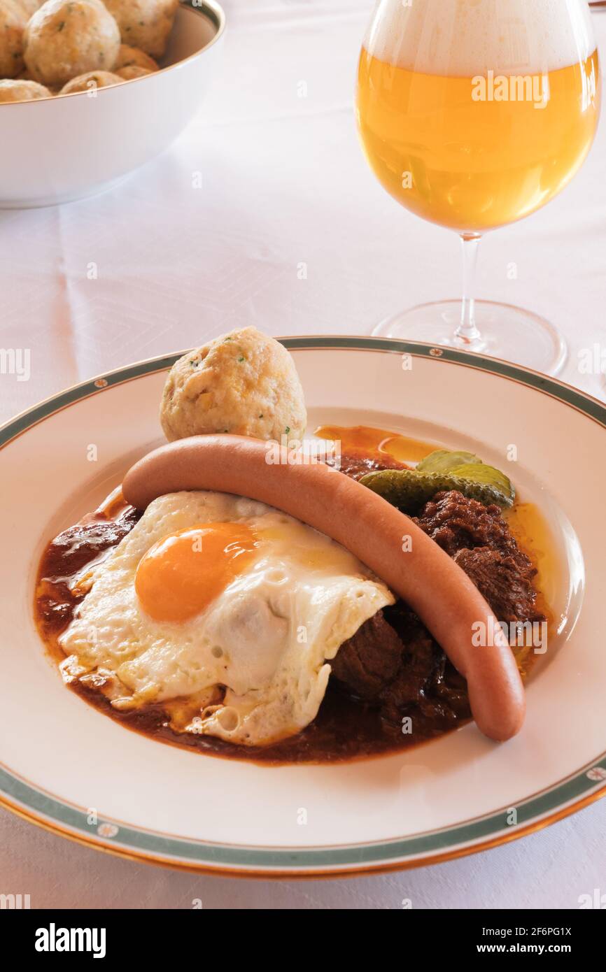 Fiakergulasch o Herrengulasch manzo viennese Goulash guarnito con un pan Dumpling, salsiccia di Francoforte, uova fritte e Gherkin su un piatto, servito con Foto Stock