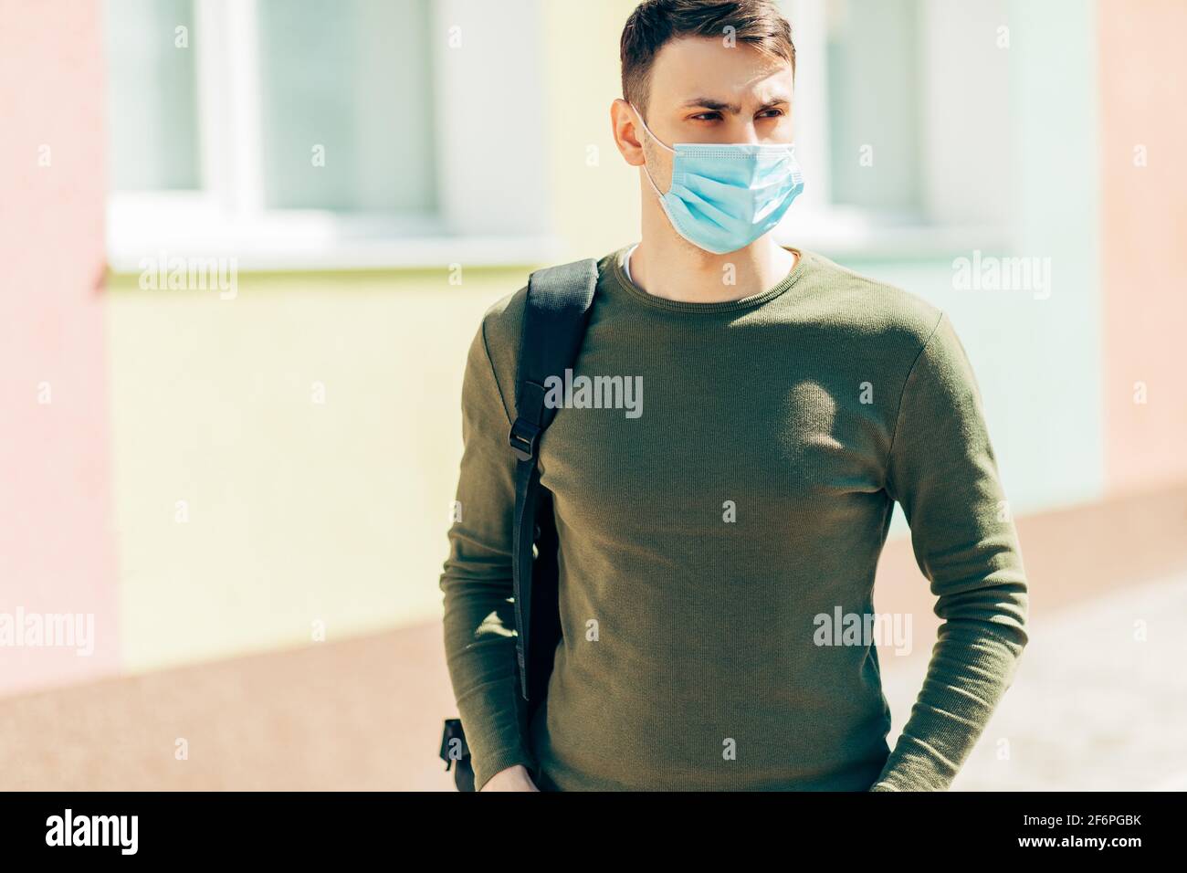 Ritratto di un giovane che indossa una maschera sulla strada durante la pandemia COVID-19, sullo sfondo di un edificio Foto Stock