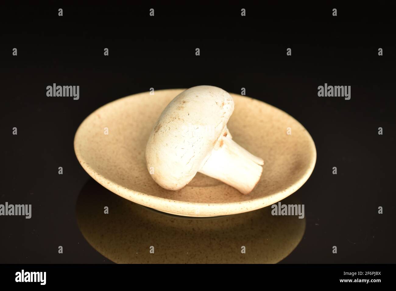 Un fungo di champignon fresco organico intero che innaffiatura la bocca su un piatto di ceramica, primo piano, su sfondo nero. Foto Stock