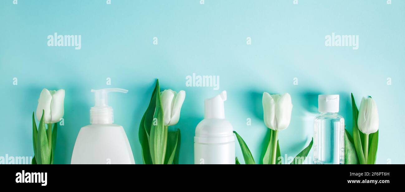 Prodotti per la cura della pelle su sfondo blu. Cosmetici naturali e tulipani bianchi. Posiziona per testo, formato banner Foto Stock