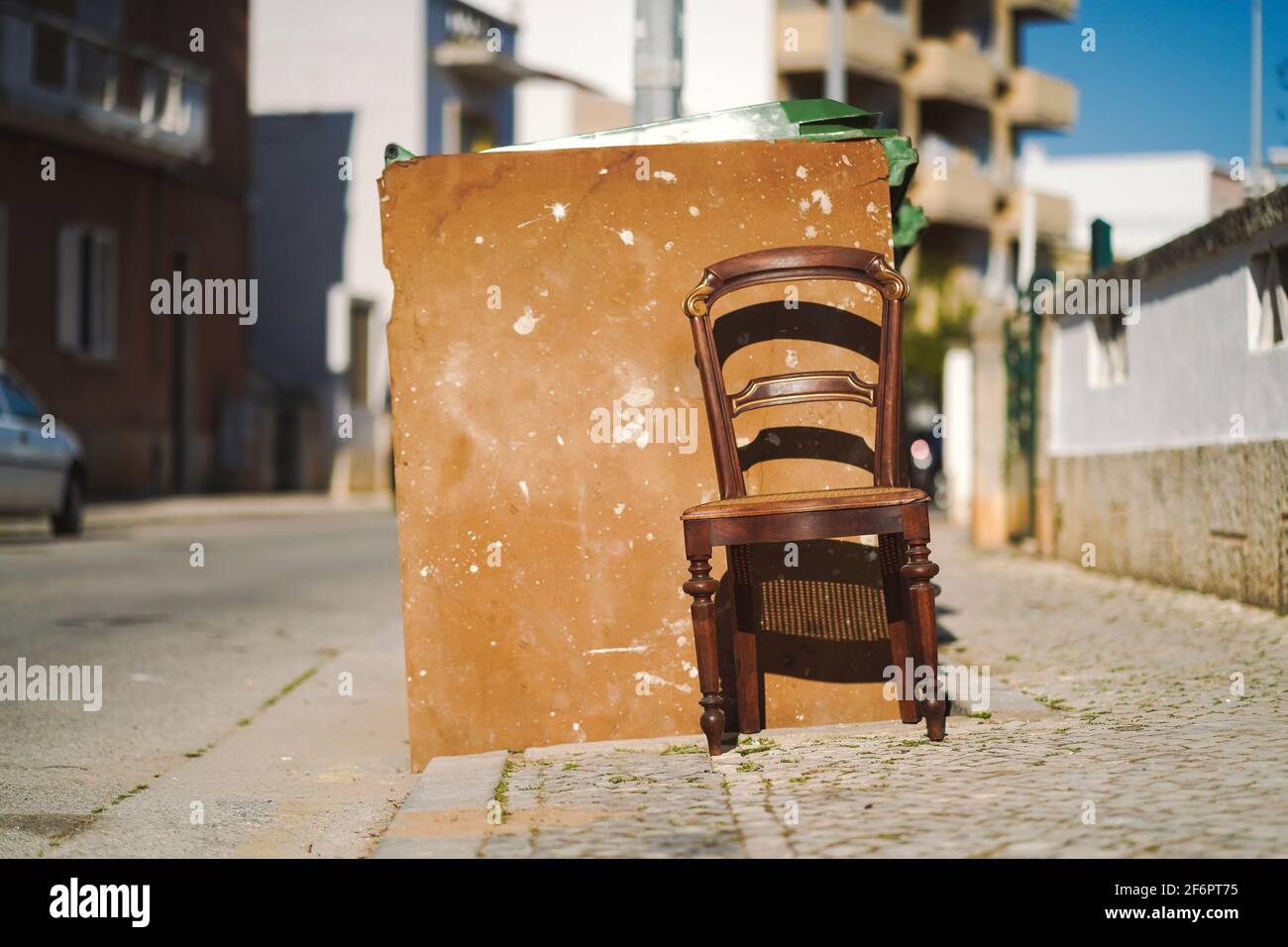 La sedia in legno vintage accanto al cestino sopra La strada pubblica nel soleggiato Portogallo Foto Stock