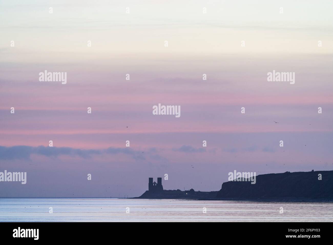 Prima luce, un cielo color pastello all'alba sul promontorio costiero di Reculver e mare calmo con le lontane torri gemelle del 12 ° secolo della chiesa in rovina Foto Stock