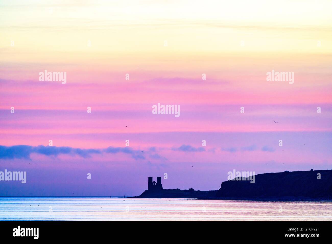 Prima luce, un cielo color pastello all'alba sul promontorio costiero di Reculver e mare calmo con le lontane torri gemelle del 12 ° secolo della chiesa in rovina Foto Stock