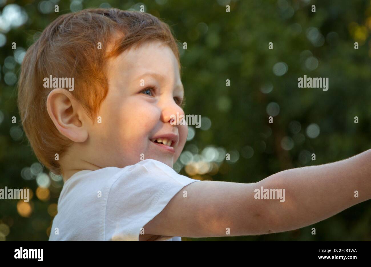Ritratto di un simpatico ragazzo rosso dagli occhi blu che indossa una t-shirt bianca in un parco giochi in una giornata di sole Foto Stock