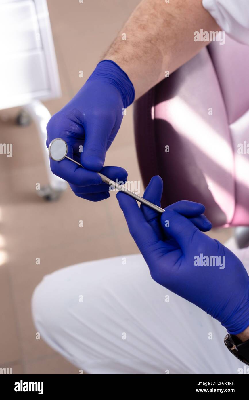 Specchio dentale in mani maschili con guanti medici blu Foto Stock