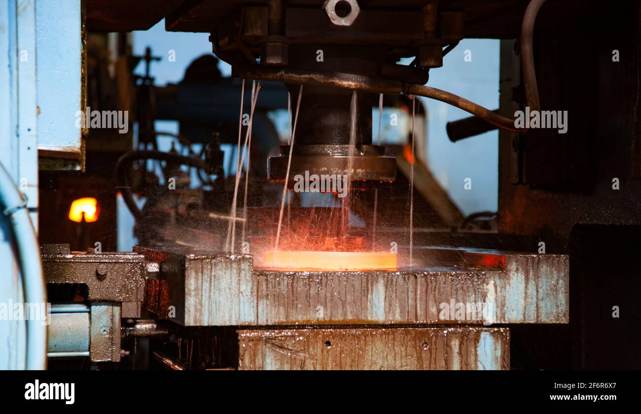Impianto di cuscinetti. Stampigliatura dell'anello del cuscinetto sulla pressa meccanica. Raffreddamento ad acqua del metallo rosso-caldo. Primo piano della foto. Steppogorsk, Kazakistan Foto Stock