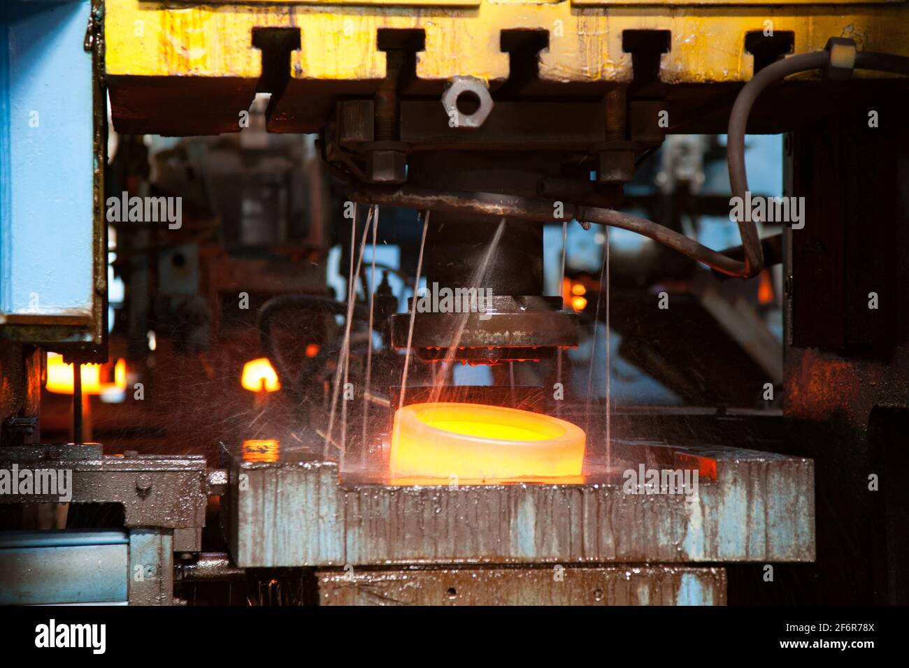 Impianto di cuscinetti. Stampaggio dell'anello esterno del cuscinetto sulla pressa meccanica. Raffreddamento ad acqua del metallo rosso-caldo. Primo piano della foto. Bassa profondità di campo. Anello di messa a fuoco Foto Stock