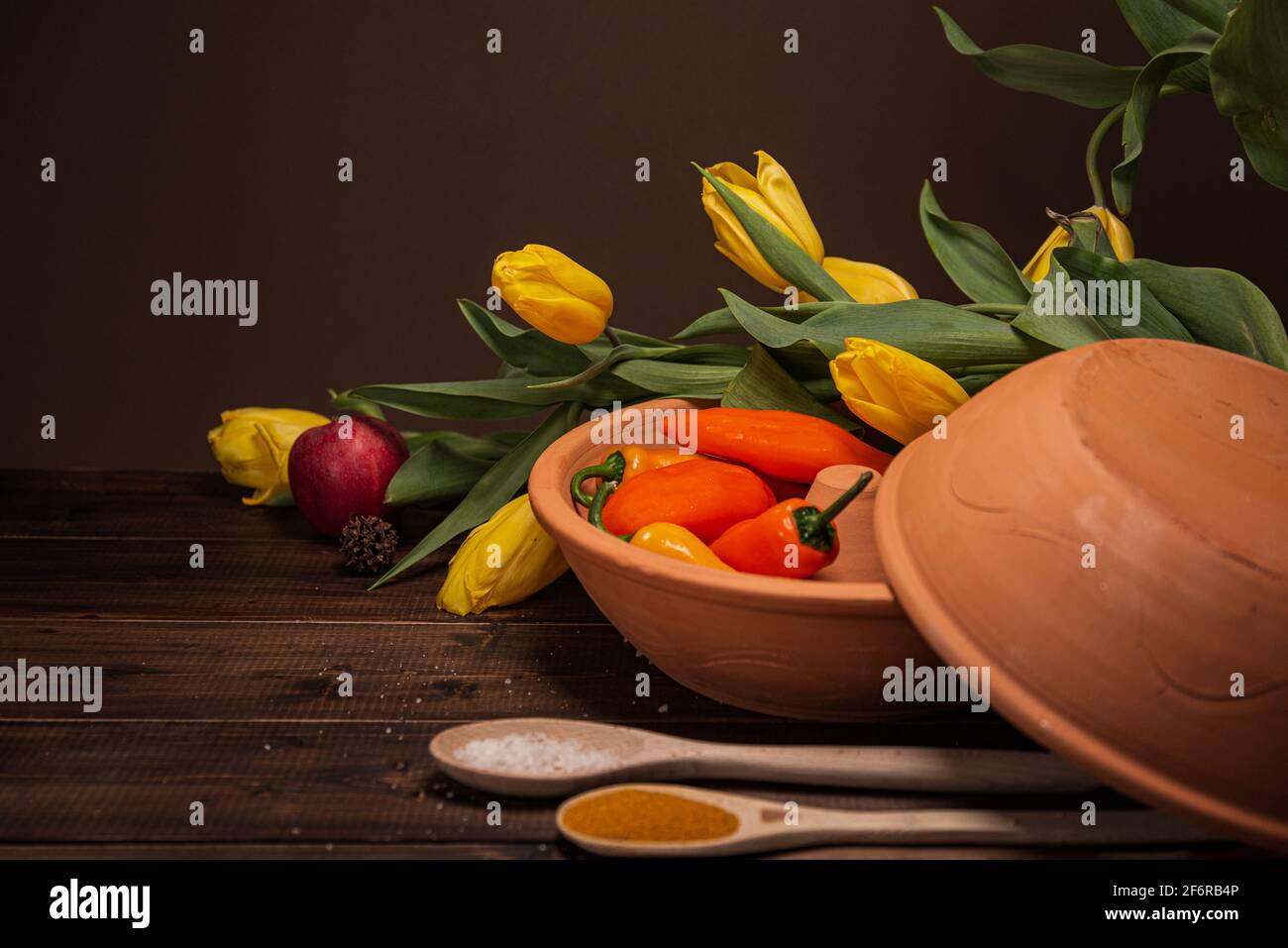 Sulla tavola con copertura in legno di colore marrone naturale, si vede una ciotola in ceramica con peperoni e arance arancioni, sullo sfondo sono tulipani, arelas, Foto Stock