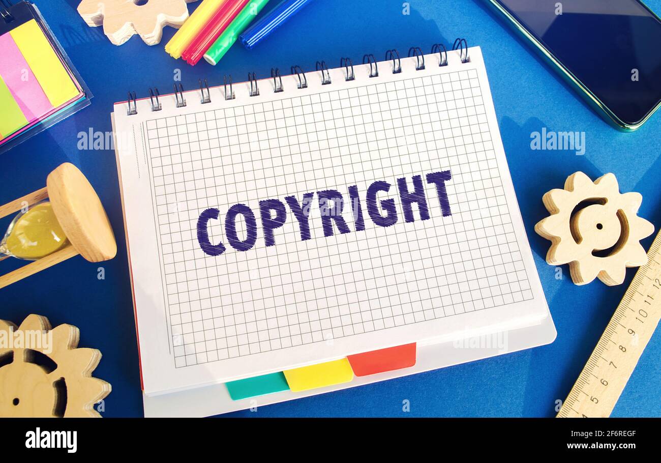 Notebook con la parola Copyright. Brevettazione. Protezione del copyright. Marchio e brevetto. La lotta contro la pirateria online. Ingranaggi, clessidra. Sfondo blu Foto Stock