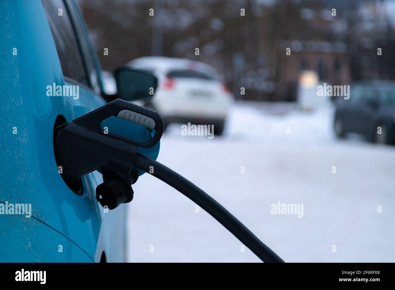 Spina di ricarica inserita in auto elettrica su fondo invernale innevato. Energia verde. Foto Stock