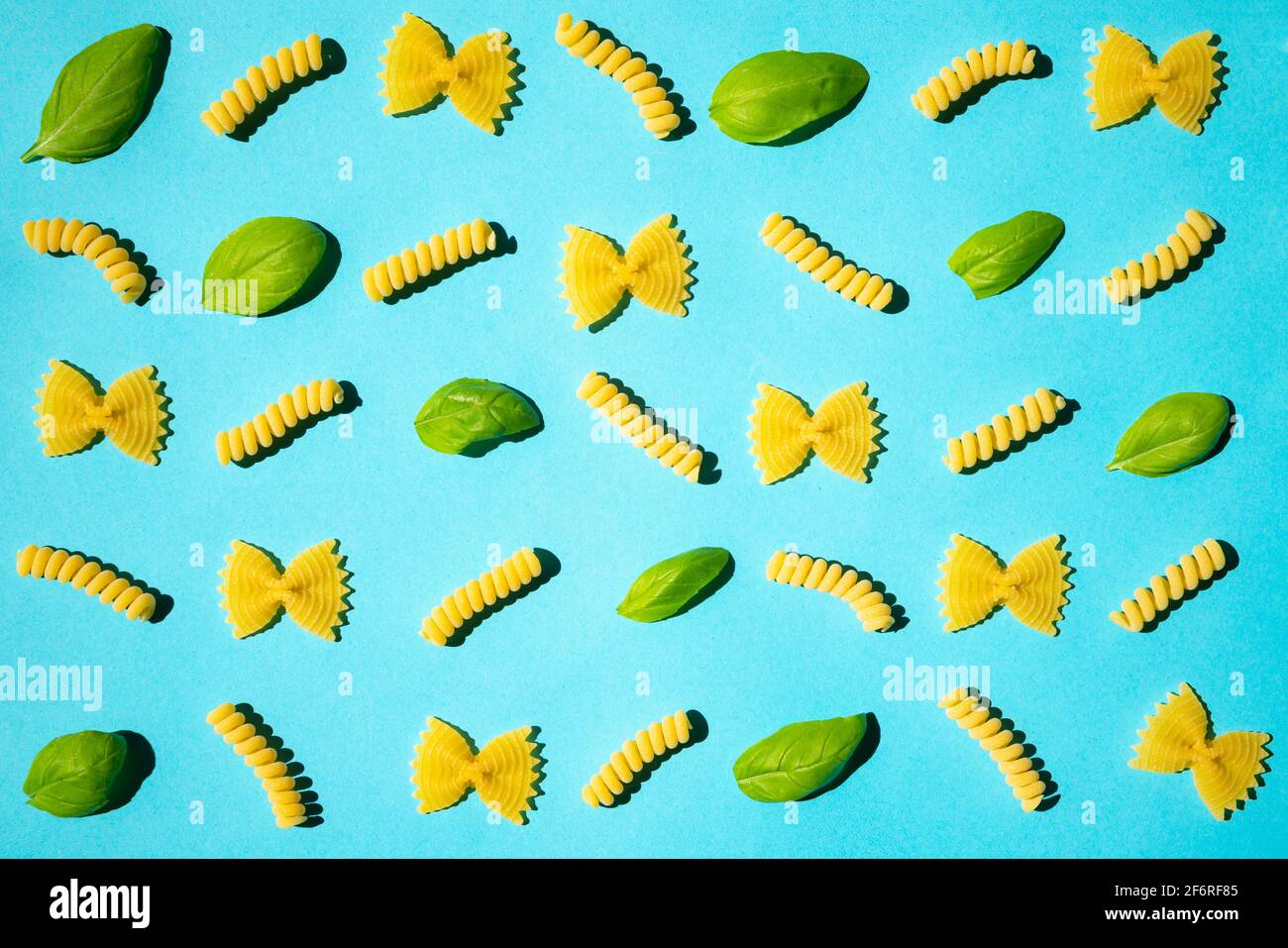 Pasta arricciata e foglie di basilico non cotti su sfondo blu. Tradizionale modello di maccheroni crudi asciutti. Nessuno Foto Stock