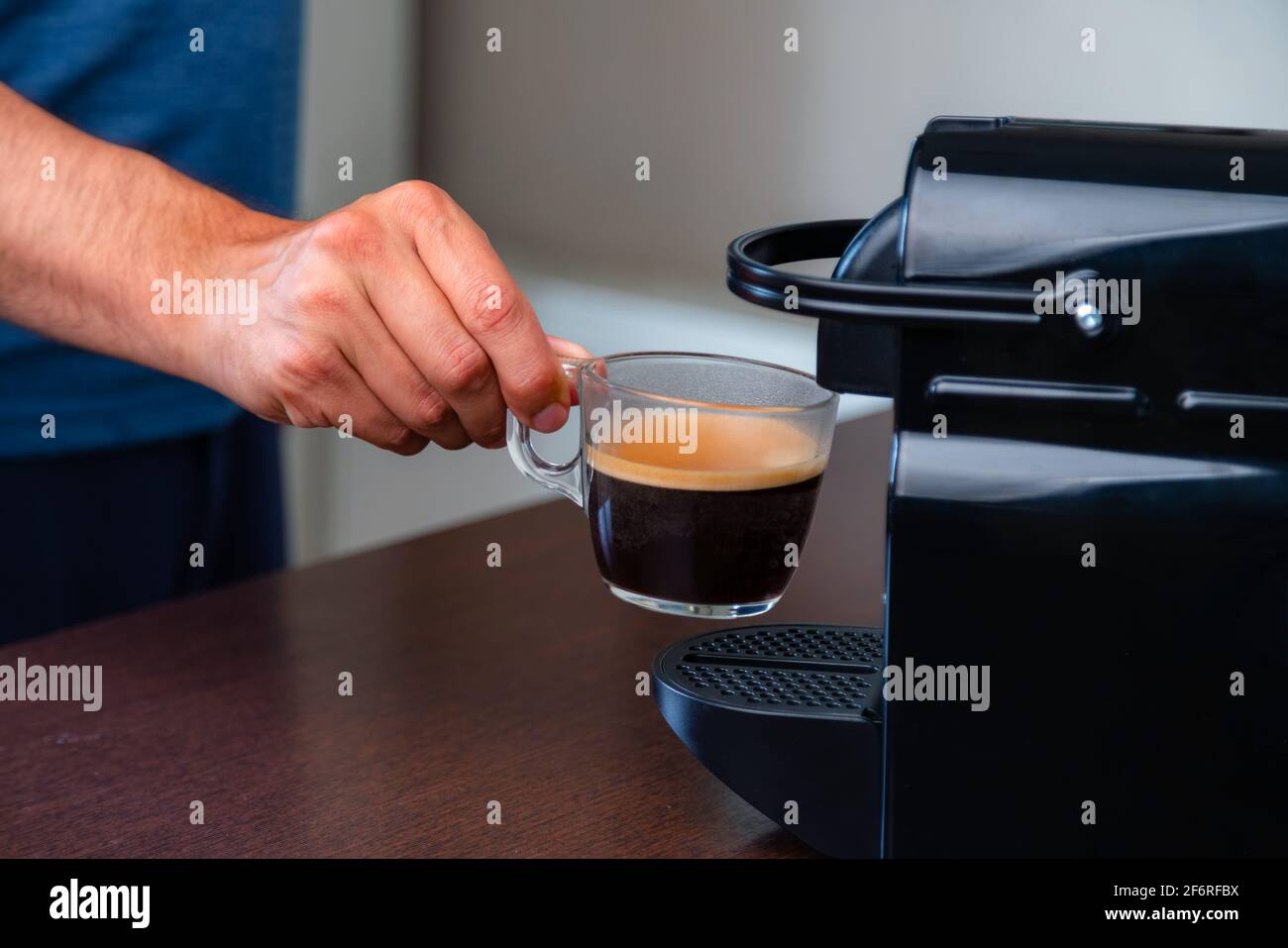Primo piano di una mano che raccoglie una tazza di caffè espresso con macchina da caffè a capsule a casa. Concetto di pausa caffè. Foto Stock