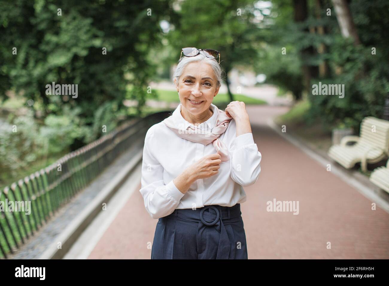 Bella donna anziana vestita con abiti eleganti camminando nel verde parco  durante il caldo tempo di sole. Bella donna sorridente e guardando la  macchina fotografica Foto stock - Alamy