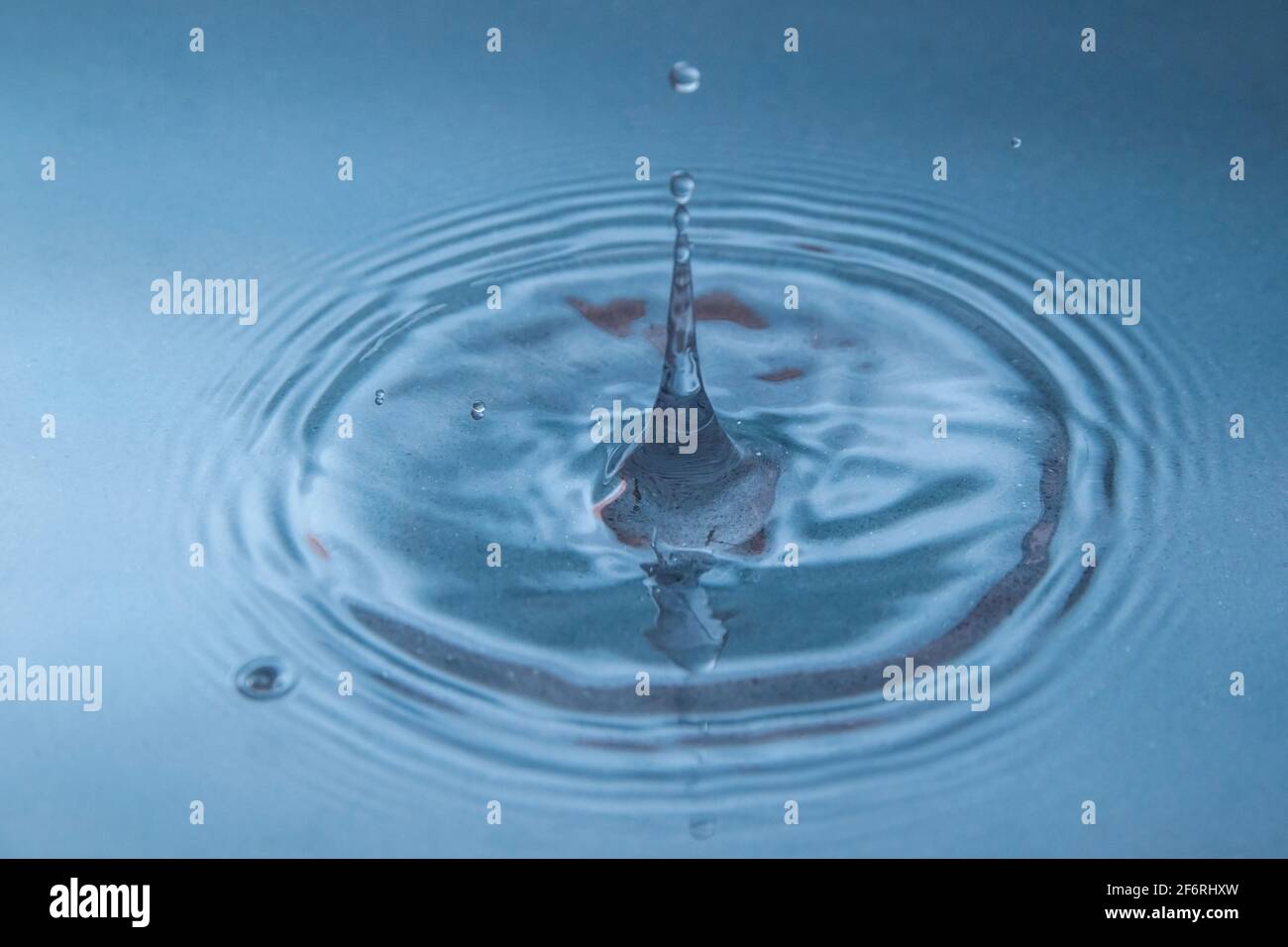 Una goccia cade nell'acqua blu e vola in su, gelando. Primo piano. Immagine di sfondo Foto Stock