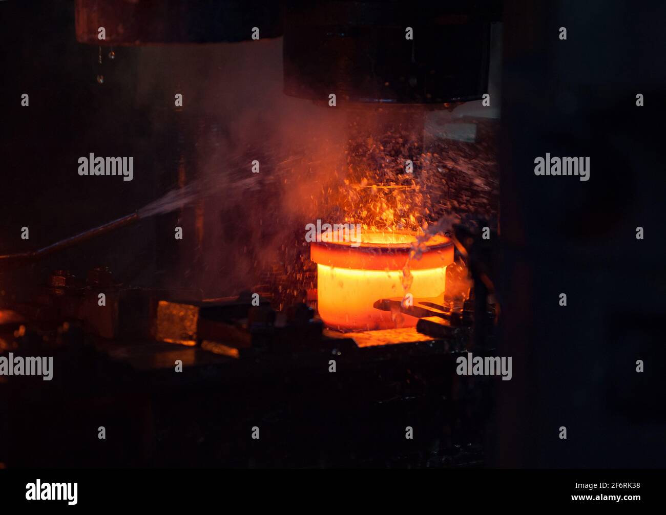 Impianto di cuscinetti. Stampigliatura dell'anello interno del cuscinetto su una pressa meccanica. Raffreddamento ad acqua del metallo. Metallo rosso-caldo. Primo piano della foto Foto Stock