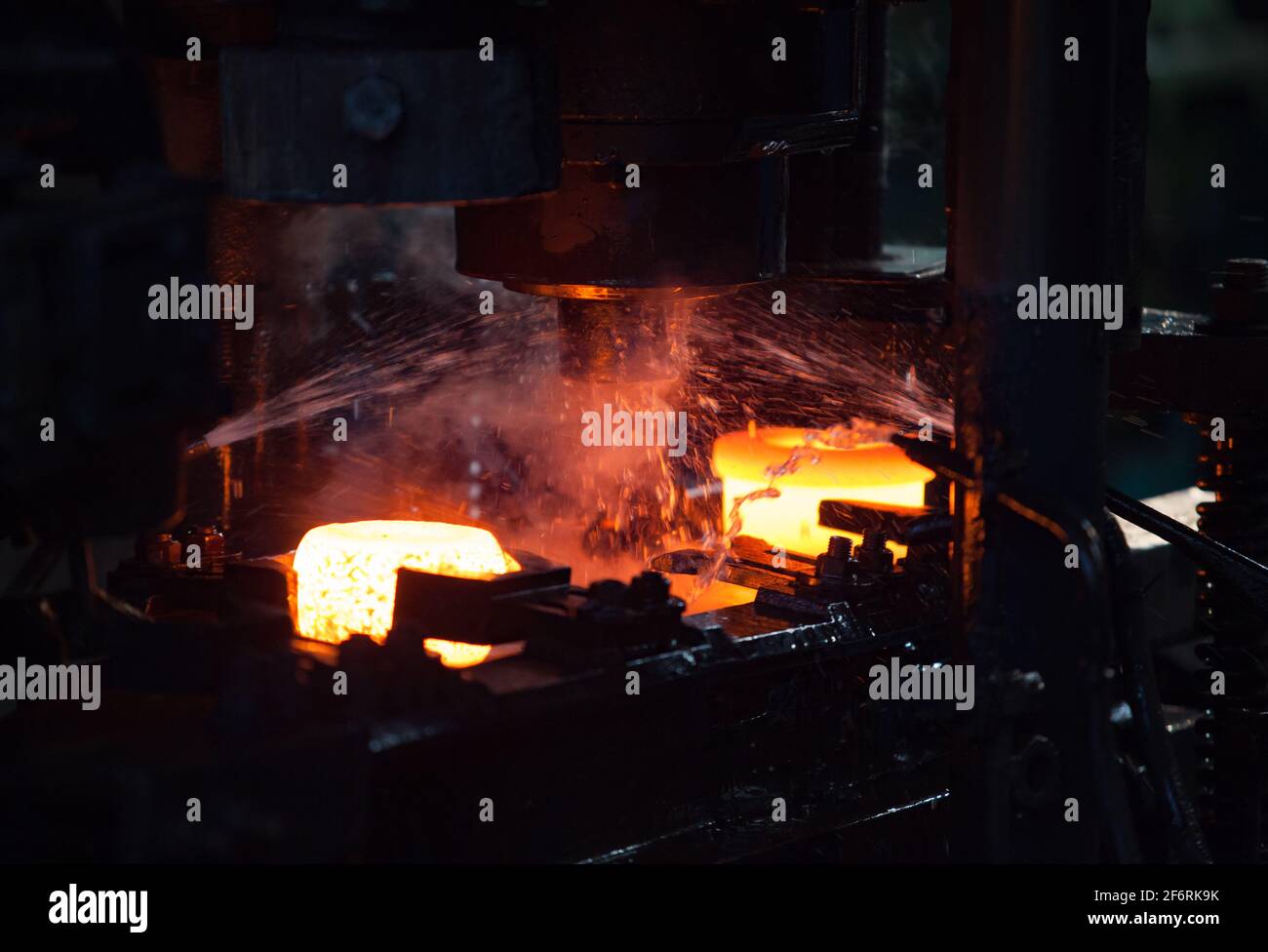 Impianto di cuscinetti. Stampigliatura dell'anello interno del cuscinetto su una pressa meccanica. Raffreddamento ad acqua del metallo.Bianco caldo Foto Stock