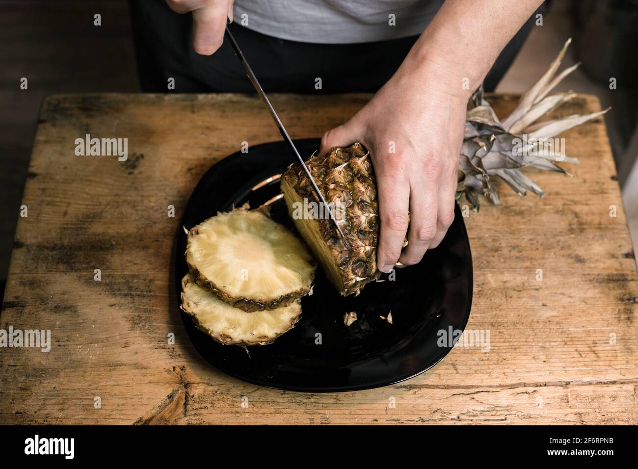 L'uomo taglia l'ananas con un coltello su un tavolo di legno Foto Stock