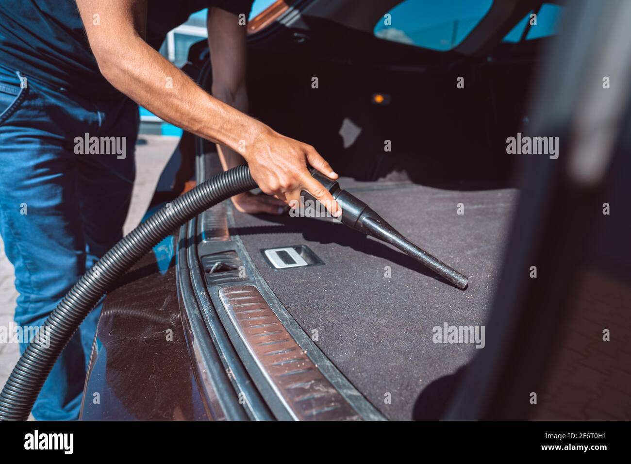 Uomo che aspira il bagagliaio di un'auto. Auto di pulizia interna con aspirapolvere presso la stazione autolavaggio self-service Foto Stock