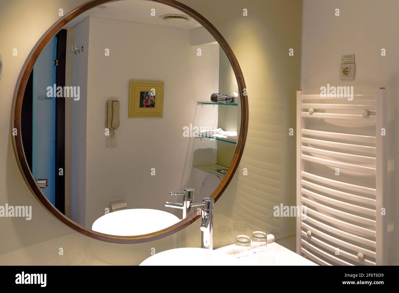Un grande specchio rotondo nel moderno bagno interno in un appartamento o hotel, con il lavandino e rubinetto riflesso Foto Stock