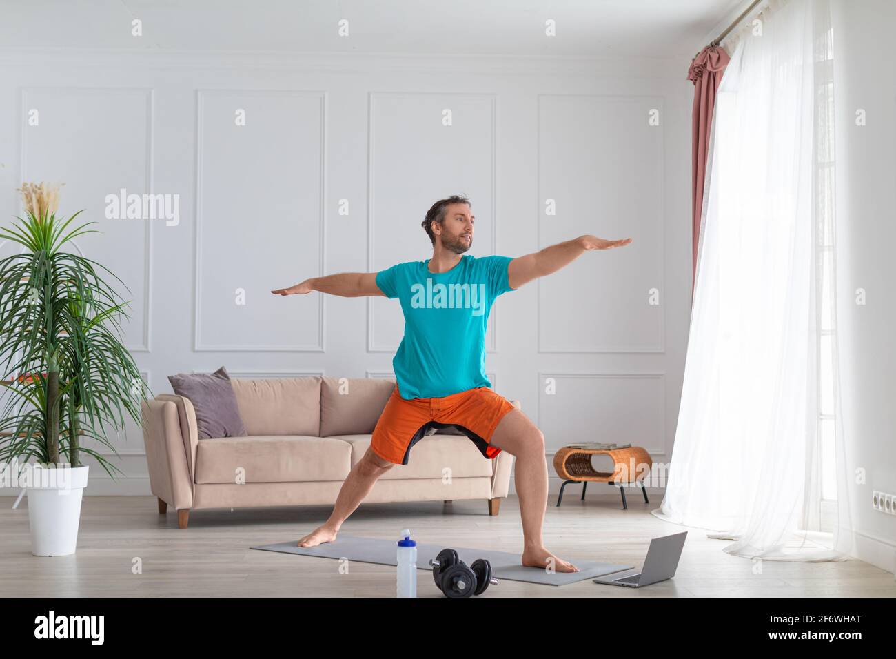 Un uomo di mezza età lavora a casa con un tutorial online. Esegue un esercizio di equilibrio davanti a un monitor portatile. Foto Stock
