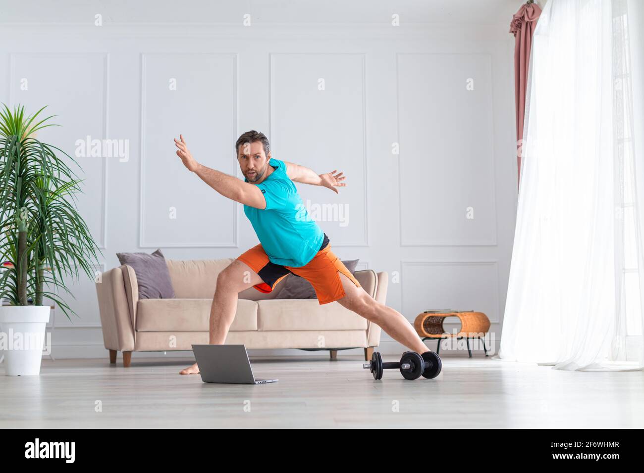 Foto PF un uomo di mezza età durante l'allenamento aerobico online. Concetto di allenamento domestico. Allenati a casa davanti al monitor del computer portatile. Foto Stock