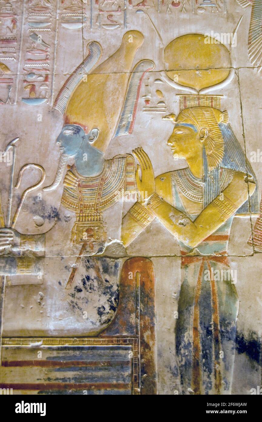 Antico egiziano dipinto e intagliato immagine degli dei Osiride seduto con Iside dietro di lui. Iside indossa la corona a corna di Hathor. Parete interna al Foto Stock