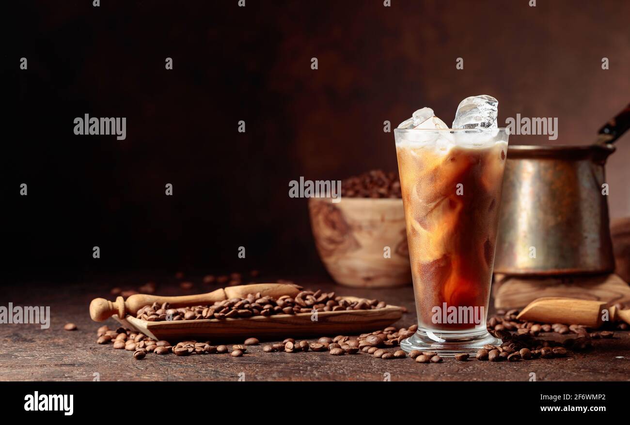 Caffè ghiacciato con panna. Bicchiere e chicchi di caffè surgelati su un vecchio tavolo marrone con utensili da cucina. Spazio di copia. Foto Stock