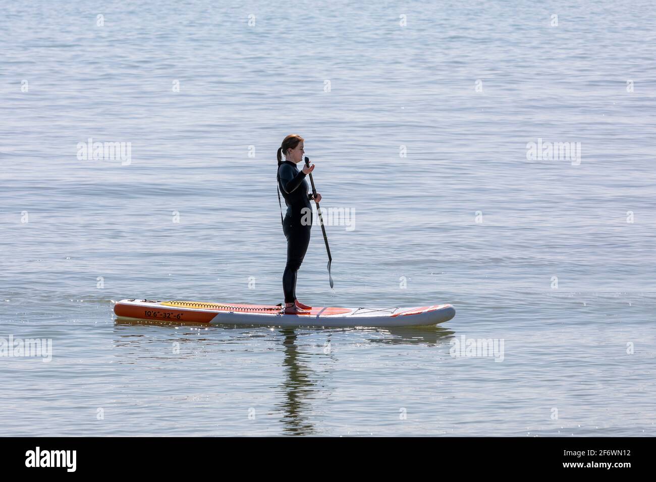 Una solitaria lady paddle boarder in piedi sulla sua tavola Foto Stock