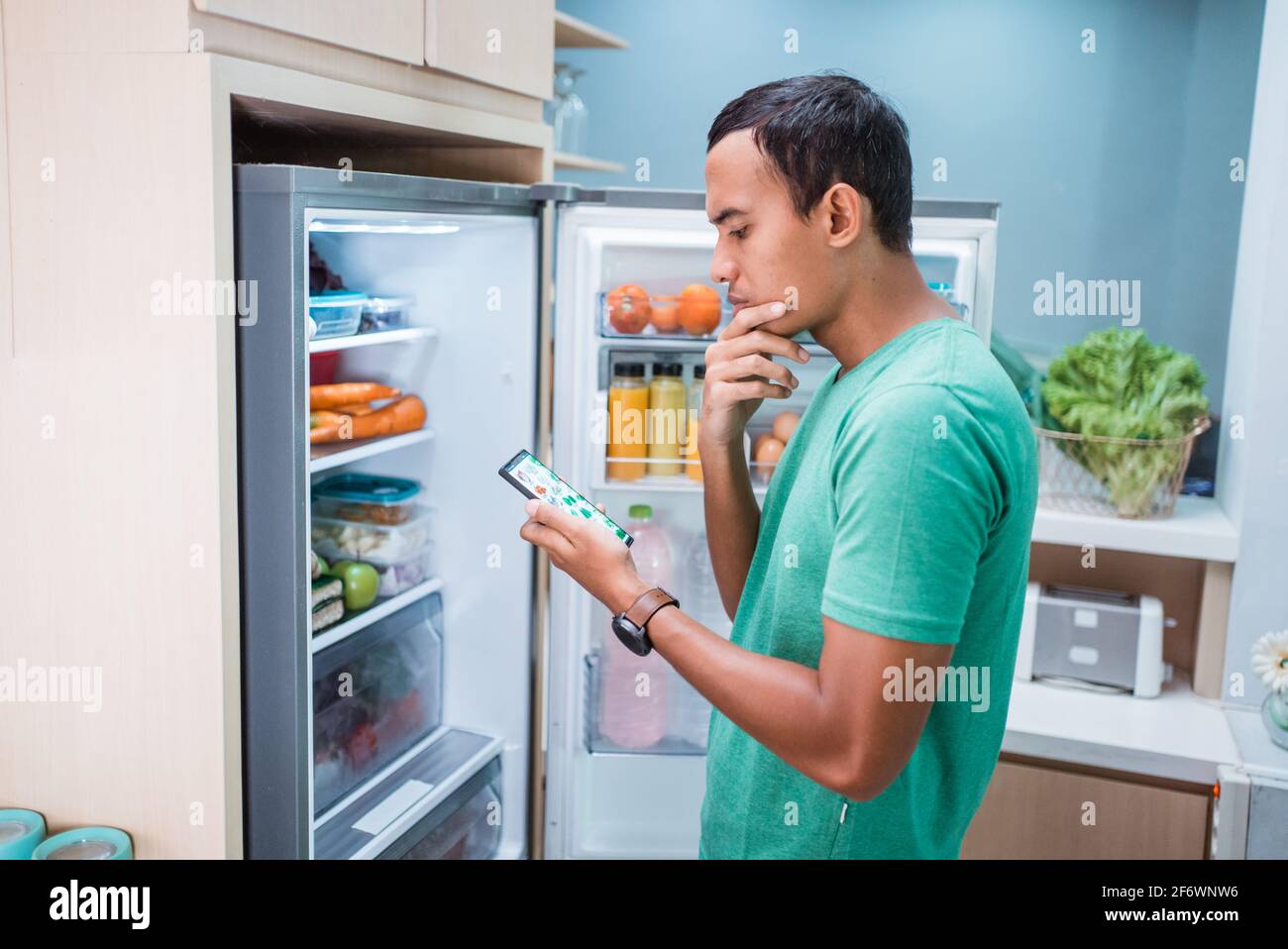 uomo in piedi davanti al frigorifero mentre lo tiene telefono cellulare  Foto stock - Alamy