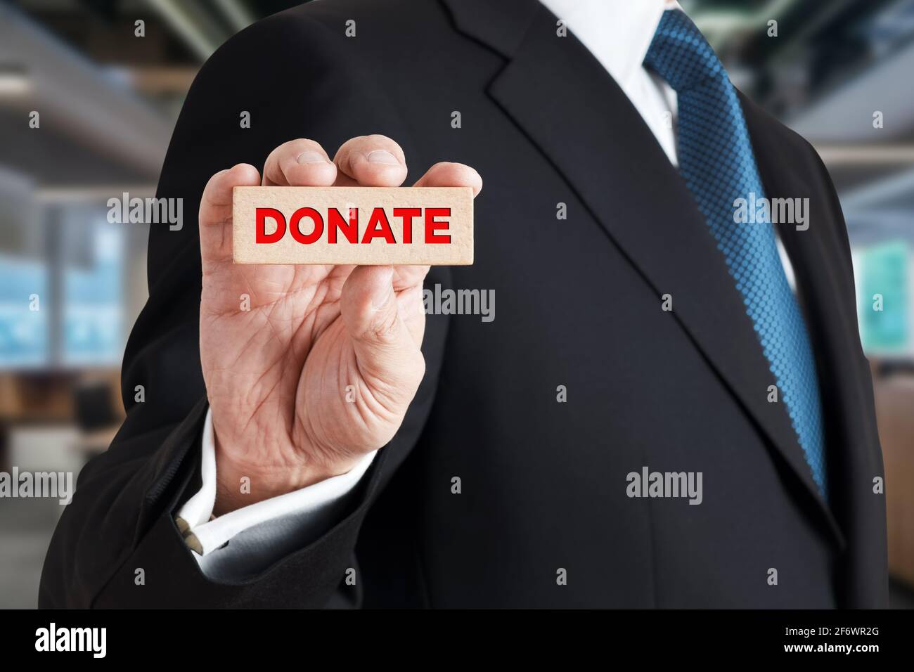 Uomo d'affari mostra un blocco di legno con la parola donate. Donazione di beneficenza nel concetto di business. Foto Stock