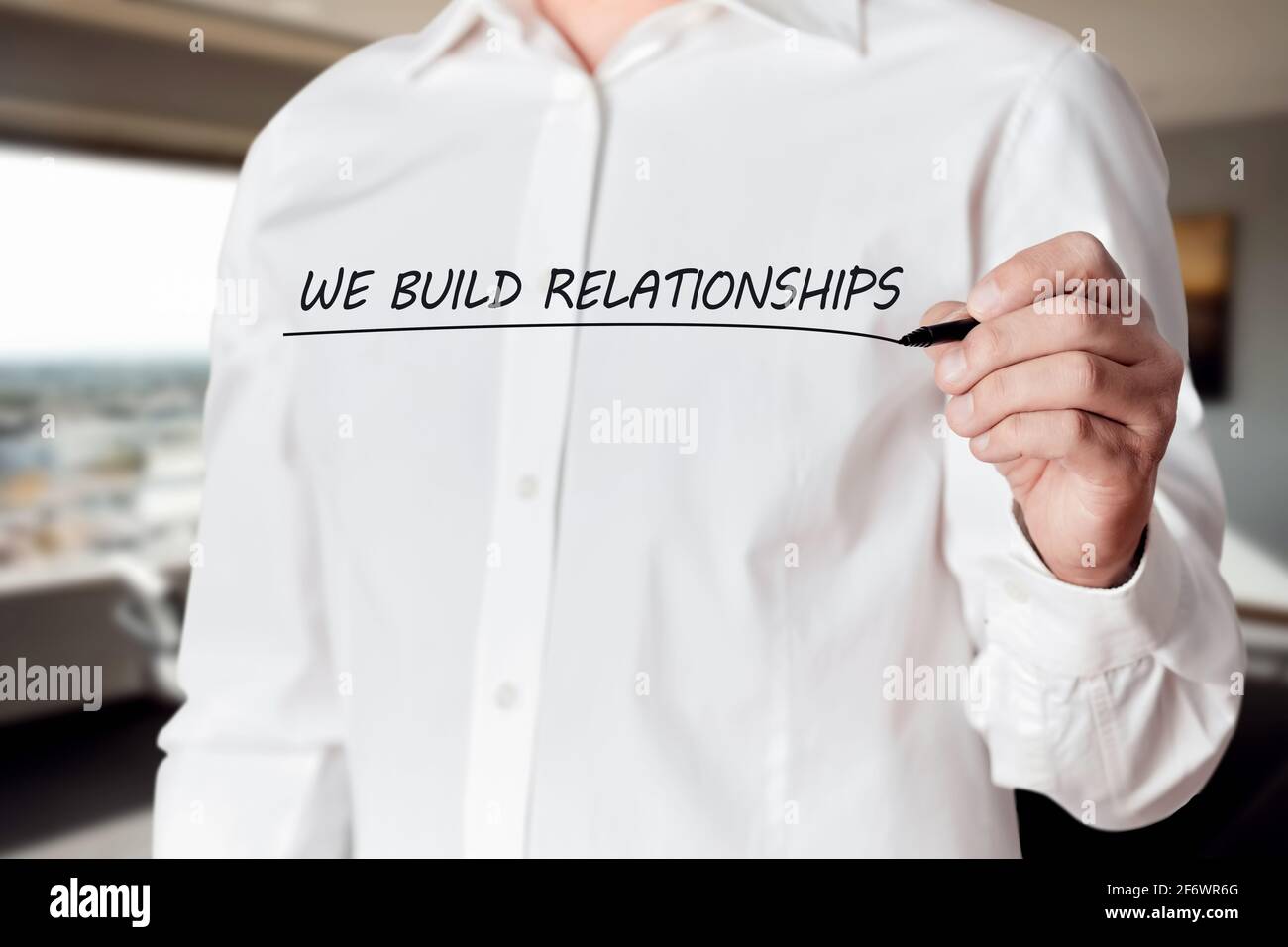 La mano dell'uomo d'affari tiene una penna e sottolinea le parole che costruiamo le relazioni su uno schermo virtuale. Rete aziendale o soddisfazione del servizio clienti Foto Stock