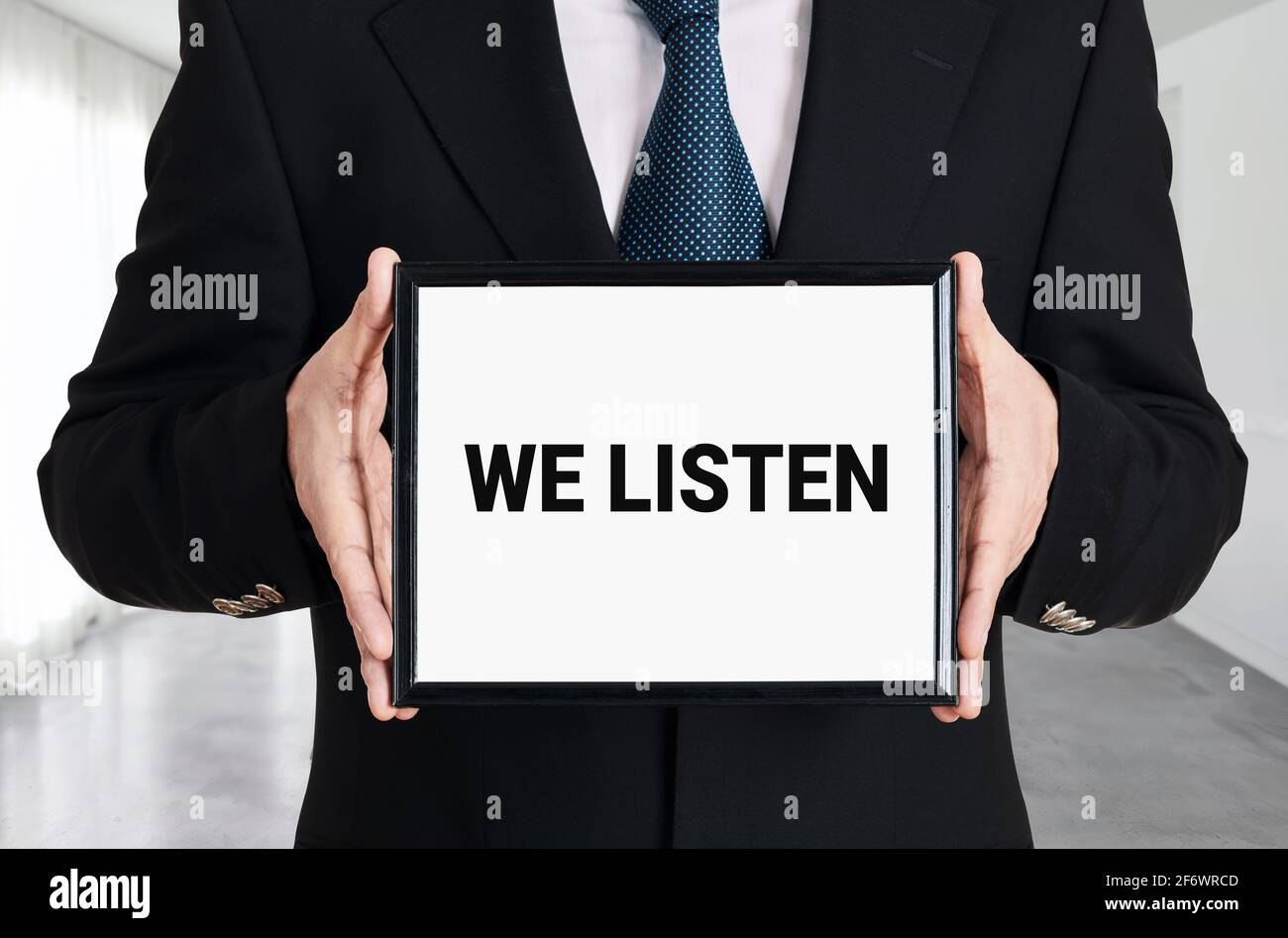 L'uomo d'affari ha un cartello con il messaggio che ascoltiamo. Concetto di assistenza clienti aziendali. Foto Stock
